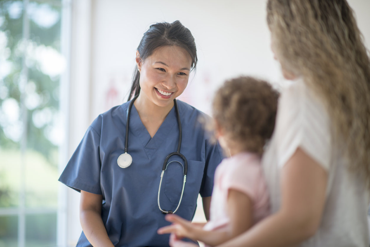 A little girl is at the doctors office for a check up. A nurse is sitting with them and talking to the mother.