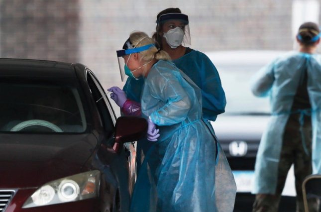 A healthcare worker performs a COVID-19 test at a drive-up testing site