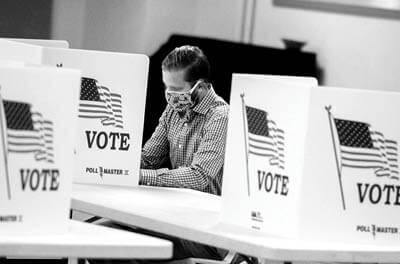 Black and white photo of a man wearing a protective mask voting at a polling site