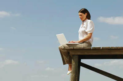 Woman sitting outside on a wooden dock using a laptop