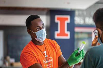 University of Illinois employee handing out a saliva test collection tube