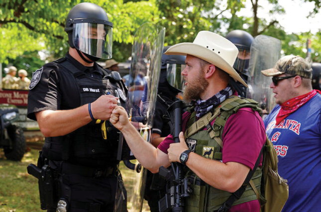 An armed far-right militia member fist-bumps a police officer in riot gear as various militia groups stage rallies at the Confederate memorial at Stone Mountain, Georgia, August 15, 2020