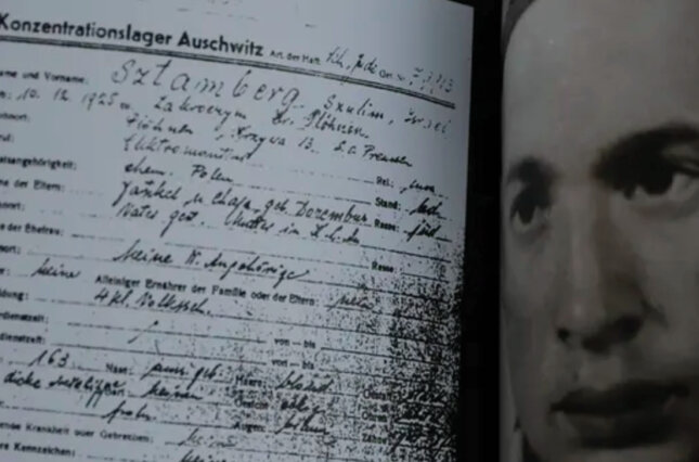 Holocaust survivor Shalom Stamberg holds a book with a photo of himself in Auschwitz, alongside a copy of his concentration camp record.