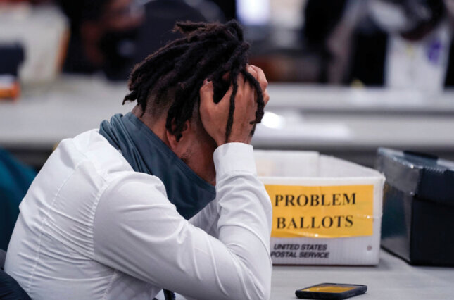 An exhausted poll worker holds his head in his hands.