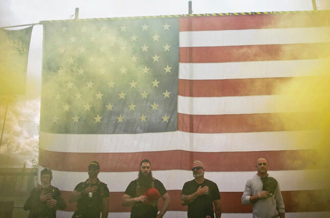 Several members of a far right militia group stand in front of a large U.S. flag