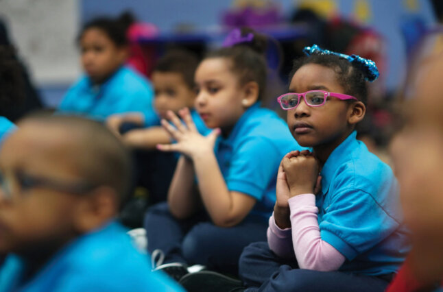 Children sit on floor hands folded