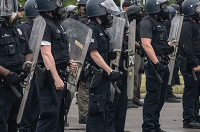 A line of police in riot gear face off with protesters