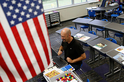 Teacher sitting in a classroom by an American flag