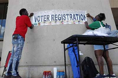 Two people put up a sign at a voter registration drive in Dallas in June 2020. Three states have enacted laws that could lead to criminal penalties or fines for some voter registration efforts.