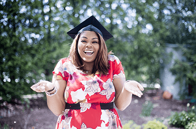 Woman standing with her hands out wearing a college graduation cap