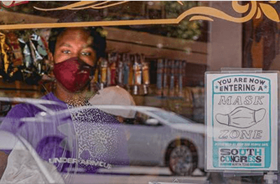 Woman looking through the window of a retail store with a sign displayed requiring customers to wear masks