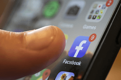 Thumb about to touch the Facebook icon on a smartphone screen