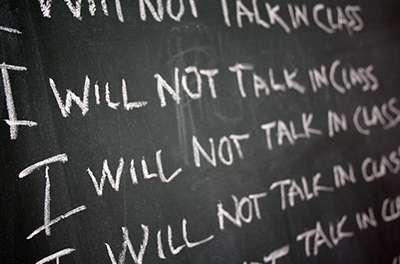 Blackboard with "I will not talk in class" written multiple times in chalk.