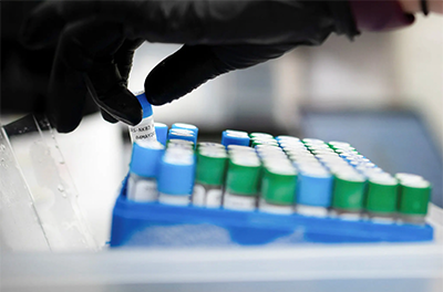 A gloved lab technician places a vile in a holder.