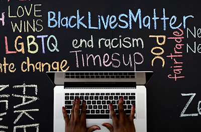 Image of a black student's hands typing on a laptop with a word cloud of race-related terms in the backround.