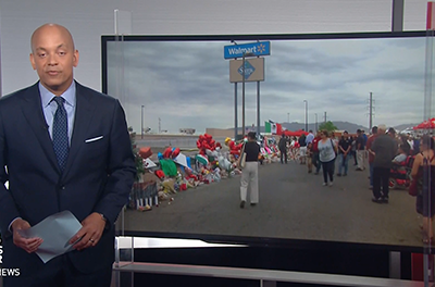 PBS News Hour reporting speaking next to a televisions displaying an image of the aftermath of the Walmart shooting.