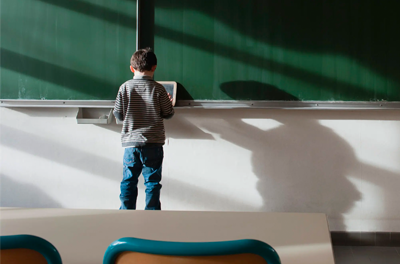 Young child standing at a chalkboard in a classroom.