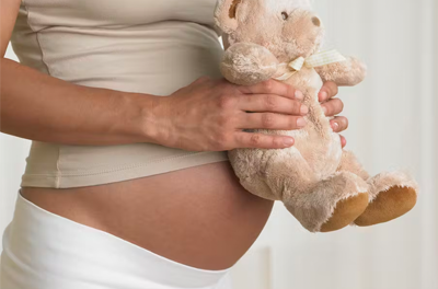 Pregnant woman holding a teddy bear.