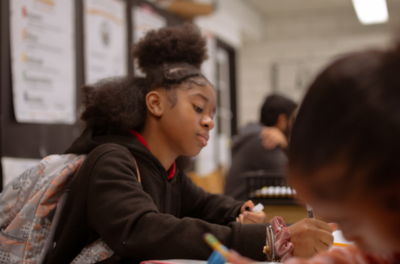 A young girl sitting at a desk writing in her notebook.